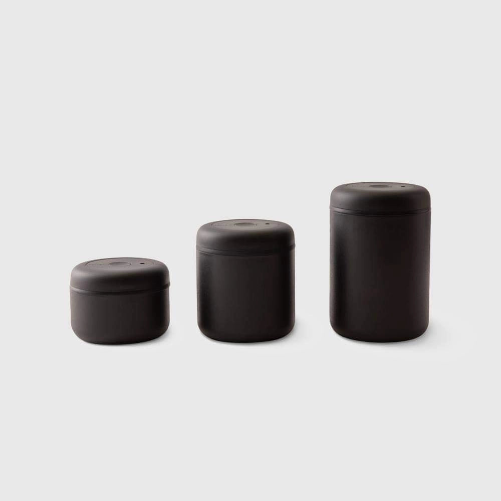 Three black cylindrical coffee bean containers of different sizes on a light gray background Fellow Atmos Coffee Bean Storage container