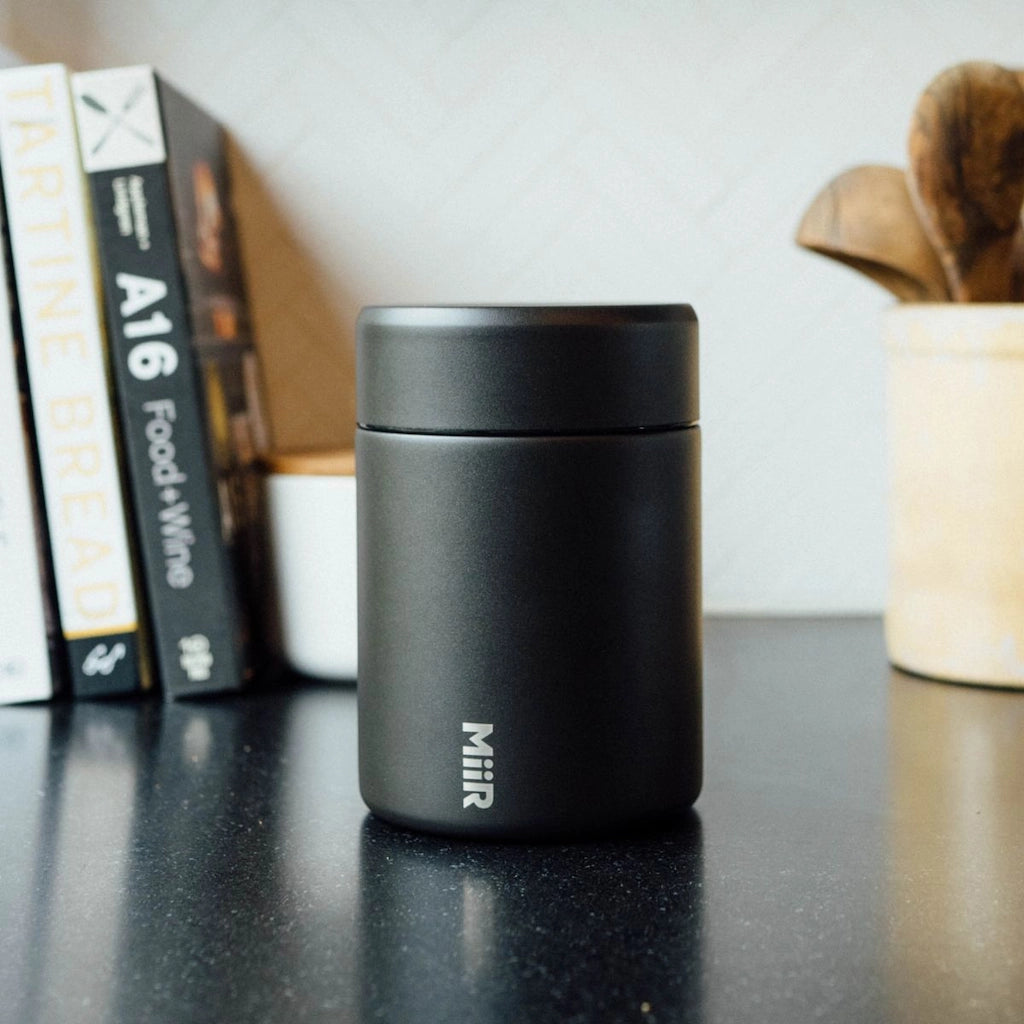 Black Miir thermos on a table with books and a container in the background